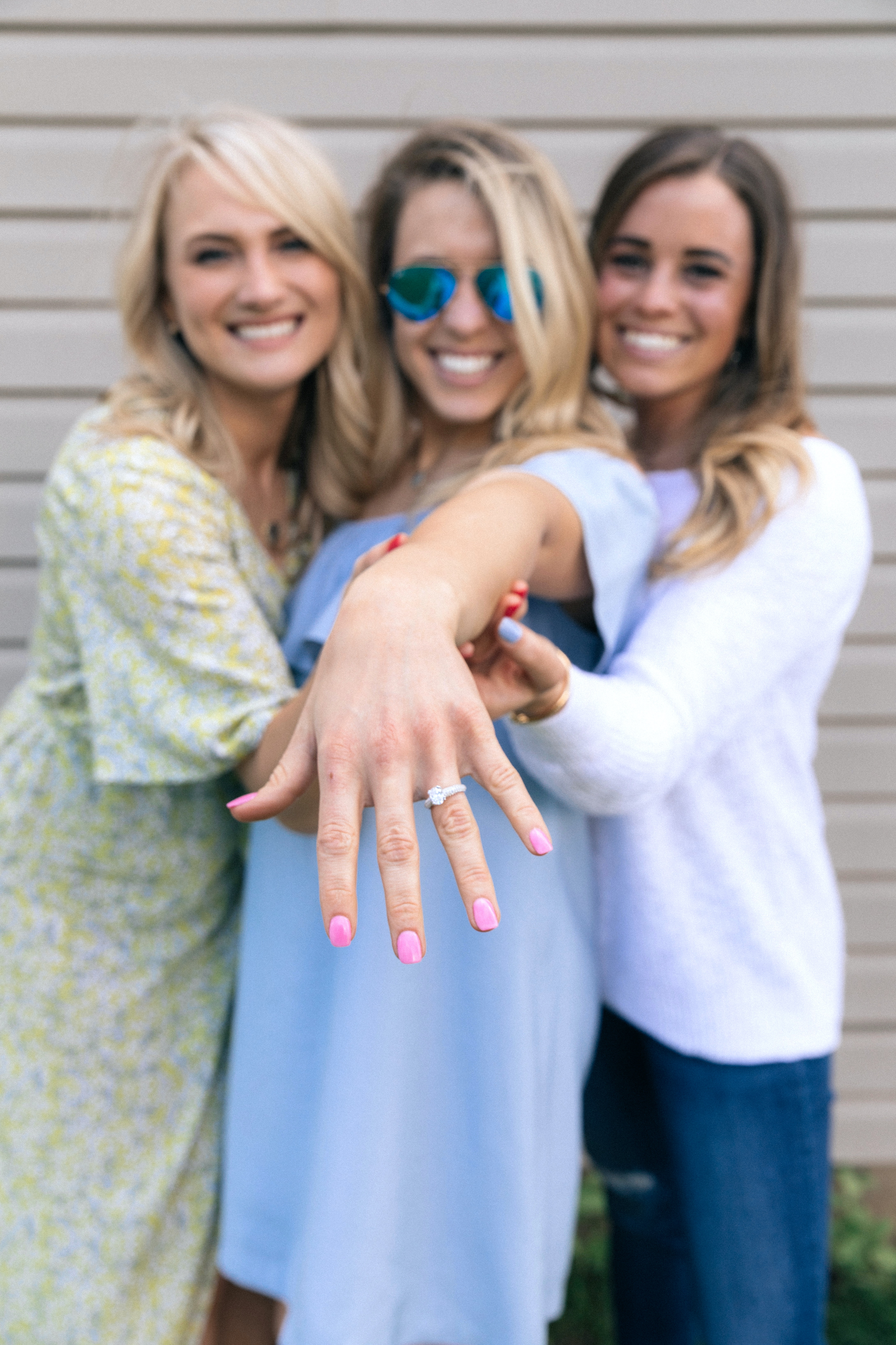 Three women stand together holding up one of their arms to display her engagement ring